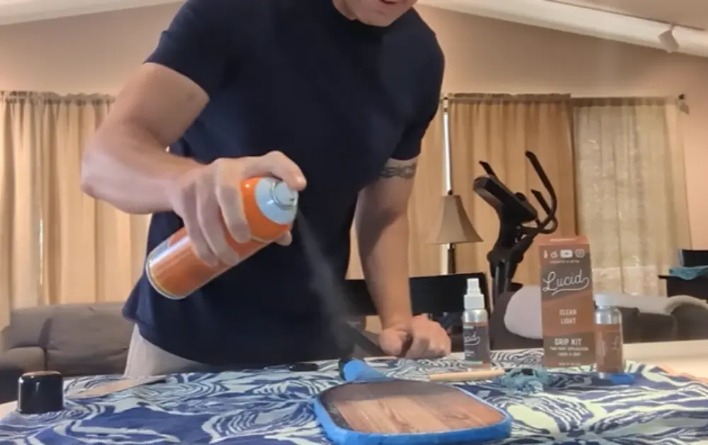Man spraying adhesive on pickleball paddle to enhance grip with added texture
